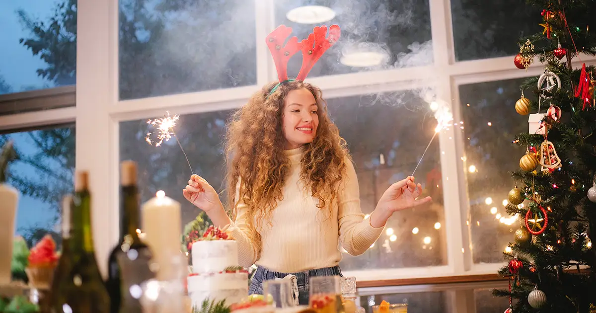 Woman wearing reindeer antlers, with sparklers in front of a decorated Christmas tree.