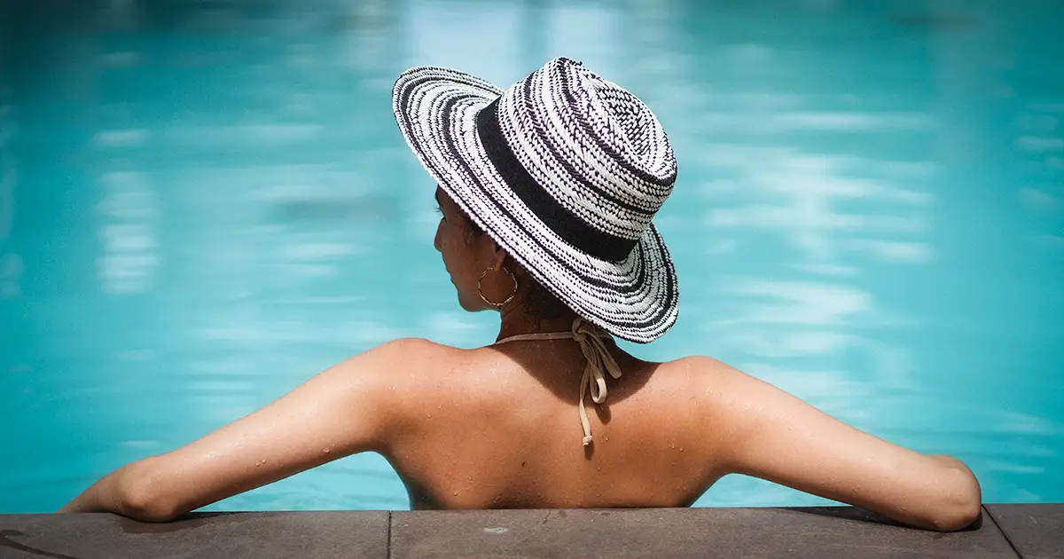 A woman in a hat reclines in a nice refreshing pool on a hot Dallas summer day.