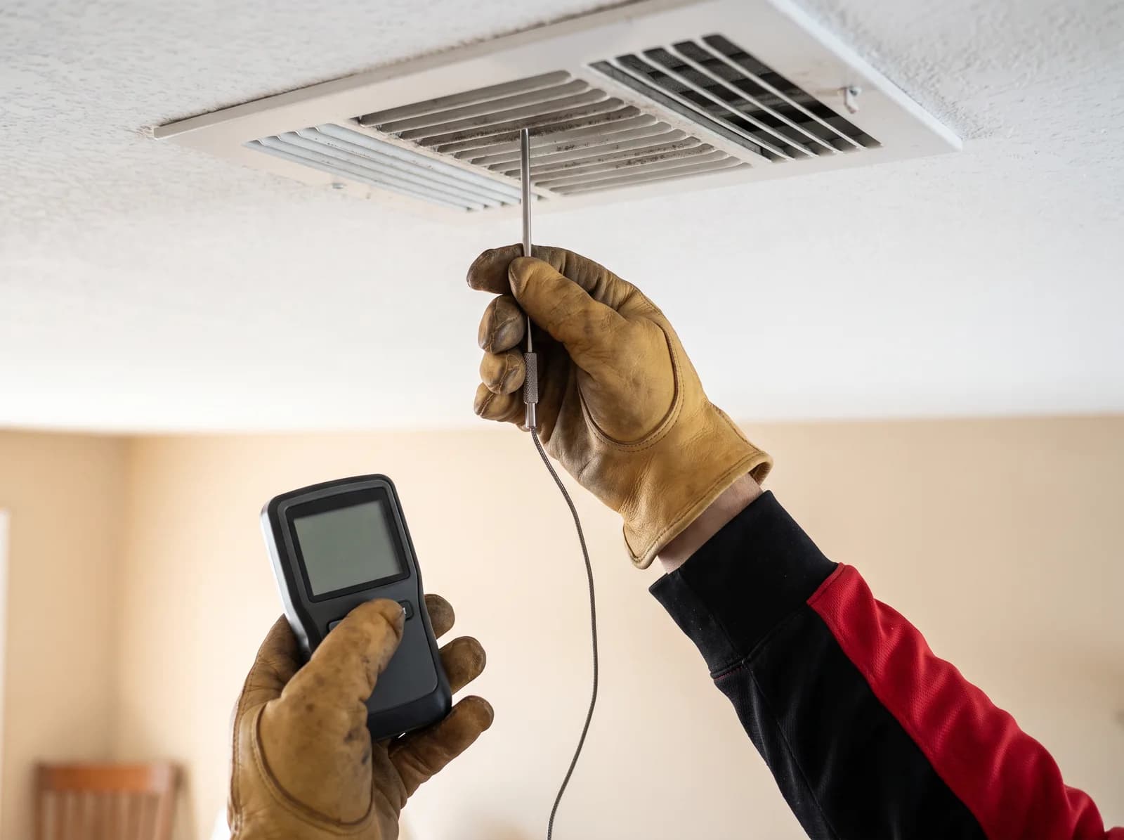 An A/C Rescue technician holding a digital thermometer probe in a ceiling supply register to read heat pump supply air temperature