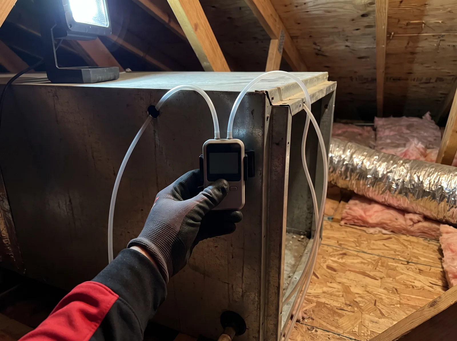 An A/C Rescue technician holding a digital manometer at an attic air handler, taking a static pressure reading across the filter slot