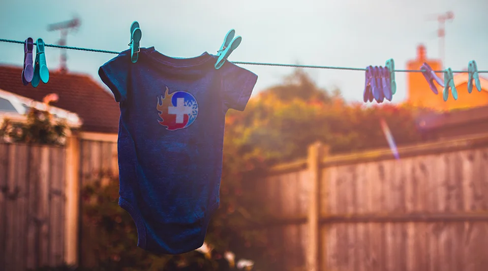 A dark blue baby's onesie with the AC Rescue logo on it, hanging on a clothesline