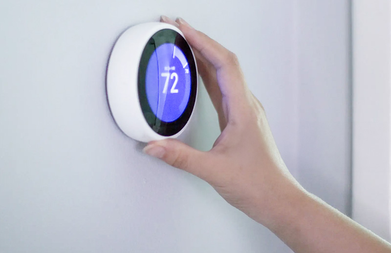 Closeup of a wall thermostat and a hand setting it to 72 degrees.