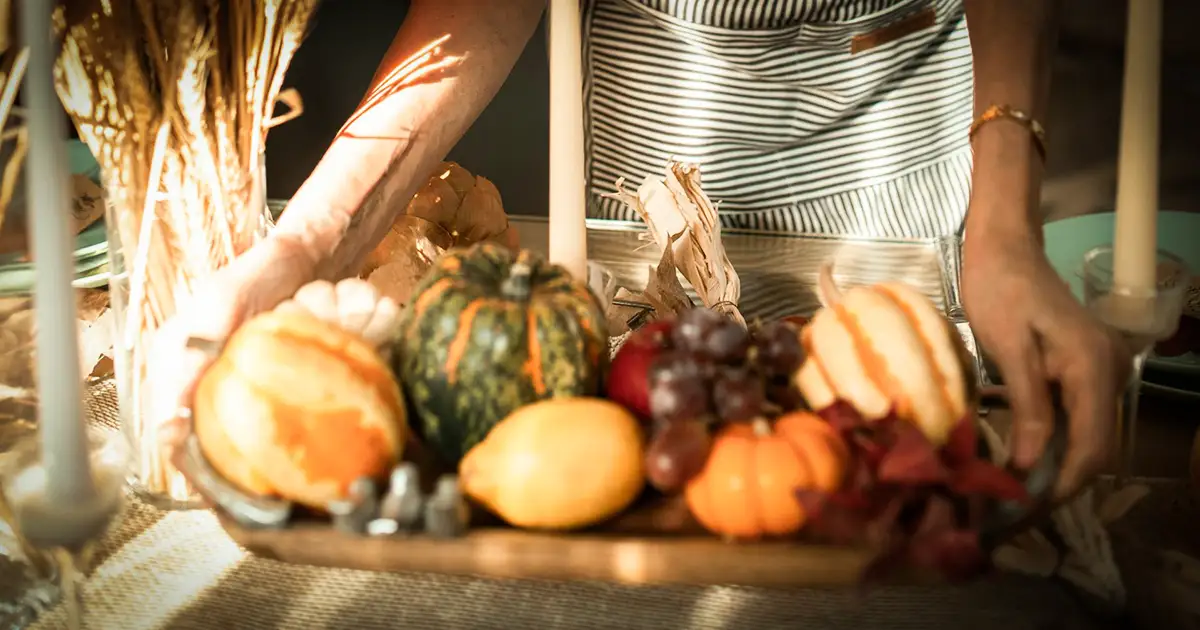 A lady bringing out a tray of assorted autumn themed vegetables.