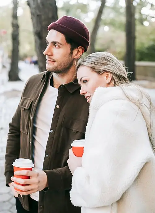A couple stands outside in the brisk fall air, enjoying cups of coffee.