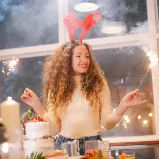 Woman wearing reindeer antlers, with sparklers in front of a decorated Christmas tree.