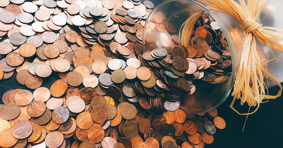 An overturned jar, spilling pennies out onto a table.